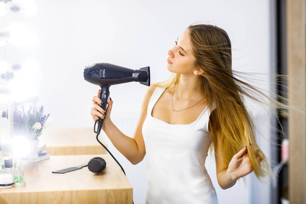 Young beautiful girl dries long hair dryer in front of mirror. - Foto, Imagem
