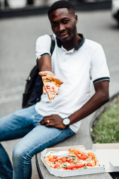 Handsome young man eating a slice of pizza outside on the street. Food concept, hungry man. - Foto, afbeelding
