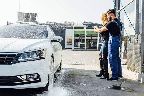 Service car wash, woman stands with master spray foam to clean engine from dirt. - Foto, afbeelding