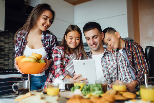 Happy father watching video on tablet computer with his two children, mother holding bowl with fresh fruits. - Φωτογραφία, εικόνα