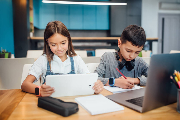 Two small friends writing homework , using smart digital tablet at modern blue classroom. - Foto, immagini