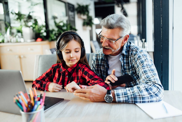 Smile attractive stylish short beard grandfather using smartphone with granddaughter. Daughter teach old man or dad using internet social media network technology with digital watch at cafe. - Φωτογραφία, εικόνα