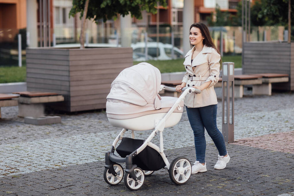 Side view of a Caucasian Mum walking on city street while pushing her toddler sitting in a pram. - Fotografie, Obrázek