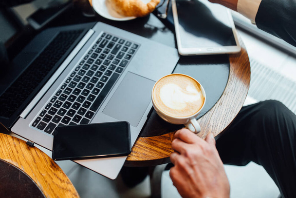 Close up photo, man have a business lunch in the modern cafe with croissant latte  and laptop and phone on wooden table. - Φωτογραφία, εικόνα