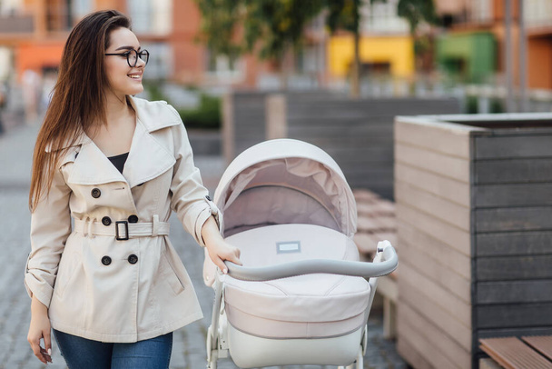 A young mother with a stroller walks through near the park. Walking with an infant in the open air. Newborn, family, child, parenthood. - 写真・画像