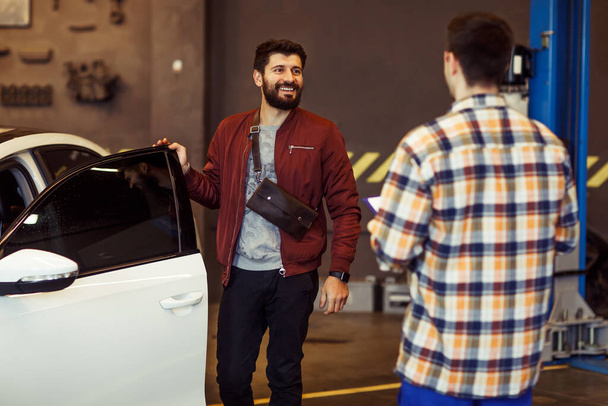 heureux client masculin ouvrant les portes de la voiture avec mécanicien dans le garage
 - Photo, image