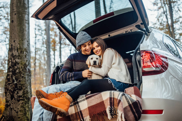 Young couple have a weekend time with their labrador retriver sitting in automobile in the autumn forest. - Фото, изображение