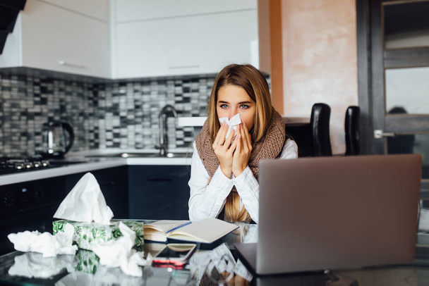 Sick business woman sitting at the table in front of the laptop at home and blows her nose. - Fotoğraf, Görsel