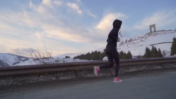 Mladá fitness žena běhá ve sněhu. Oblouk svobody v pozadí s barevnými mraky na západě slunce - Záběry, video