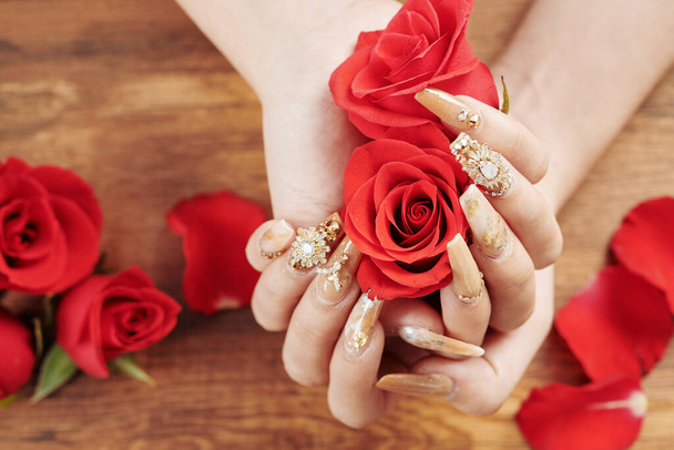 Close-up image of woman with fancy manicure holding red rose buds - Photo, Image