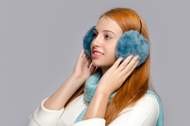 Portrait of a beautiful red hair woman wearing blue ear muffs. Woman dressed for winter - 写真・画像