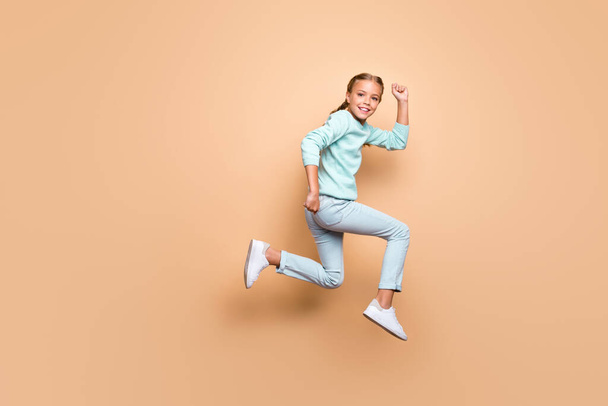 Full body photo of pretty little girl in casual clothing running jumping up high isolated over pastel color beige background - Foto, immagini