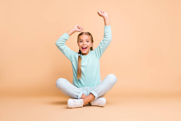 Goal. Full body photo of beautiful little lady raise fists watching sport match excited fan sit floor legs crossed wear blue sweater jeans footwear isolated beige color background - Фото, изображение
