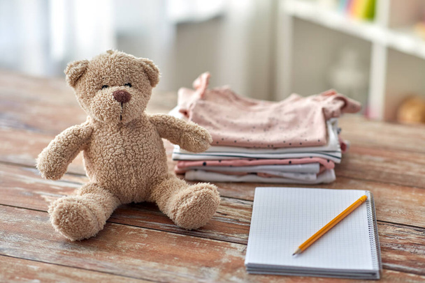 baby clothes, teddy bear toy and notebook - 写真・画像
