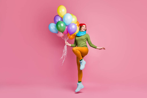 Full length photo of cheerful millennial girl jump hold many air helium balloons look copyspace enjoy winter festive anniversary wear footwear pants isolated over pink color background - Fotó, kép