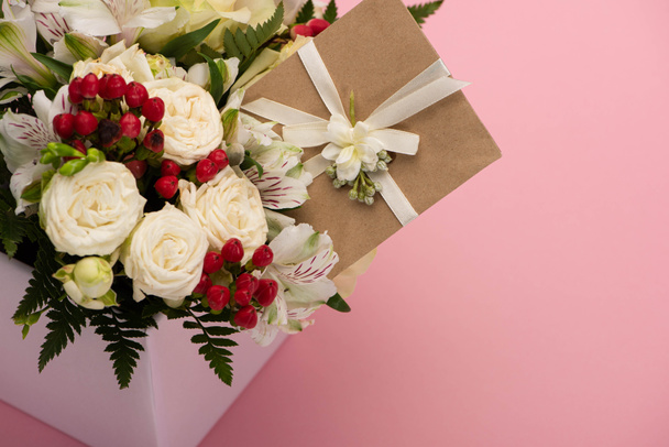 Blumenstrauß in festlicher Geschenkbox mit Grußkarte auf rosa Hintergrund - Foto, Bild