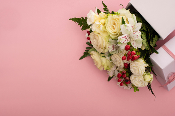 top view of bouquet of flowers in festive gift box with bow on pink background - Foto, immagini