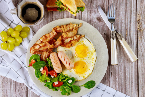 Petit déjeuner savoureux avec œufs, saucisses, bacon, pain grillé et tasse de café
. - Photo, image