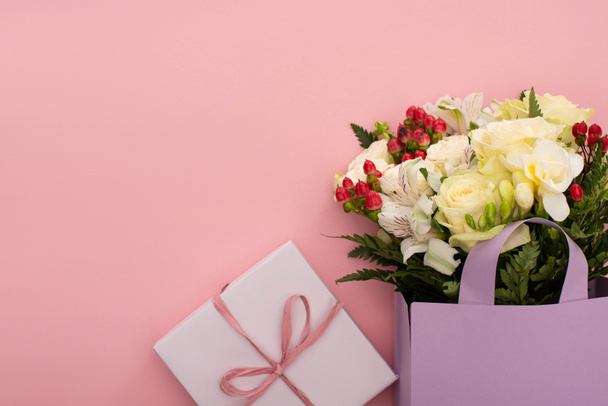 top view of bouquet of flowers in violet paper bag near gift box on pink background - Foto, afbeelding