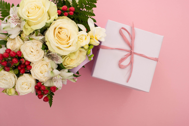 top view of bouquet of flowers and festive gift box with bow on pink background - Zdjęcie, obraz