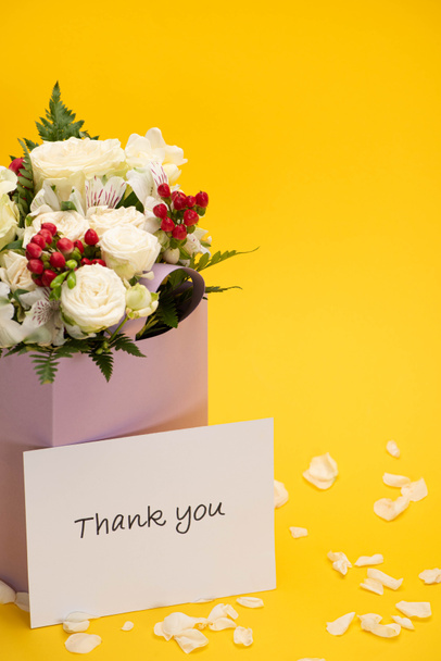 spring fresh bouquet of flowers in violet paper bag near scattered petals and thank you greeting card isolated on yellow - Photo, Image