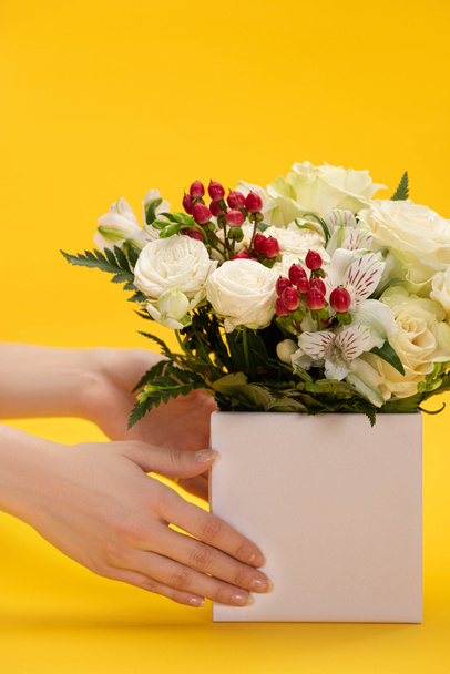 cropped view of woman holding spring fresh bouquet of flowers in box on yellow background - Foto, Imagem