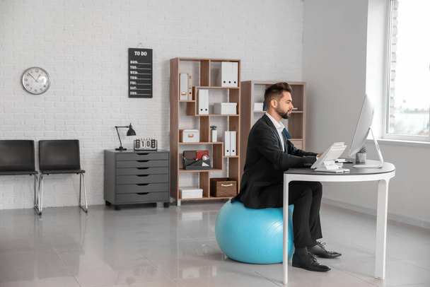 Businessman sitting on fitness ball while working in office - Foto, afbeelding