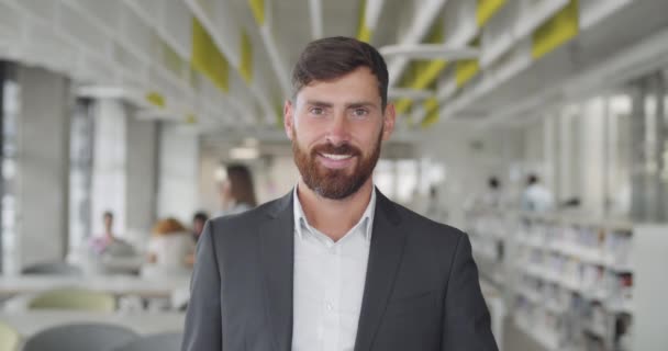 Portrait of cheerful adult businessman standing in office room. Happy male office worker looking to camera and smiling. Concept of people and workspace. Blurred background. - Materiał filmowy, wideo