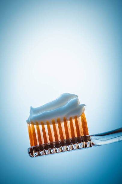 Cepillo de dientes de plástico con pasta de dientes blanca sobre un fondo azul. Vista lateral
 - Foto, Imagen