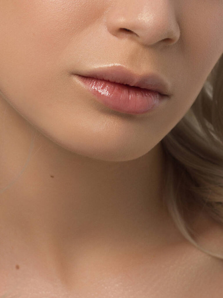 Sexual full lips. Natural gloss of lips and woman's skin. The mouth is closed. Increase in lips, cosmetology. Pink lips and long neck. Gentle pure skin and wavy blonde hair. - Photo, Image