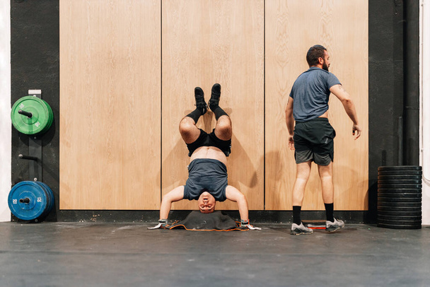 Zwei Männer trainieren am Boden in einer Turnhalle mit Handstandwand - Foto, Bild