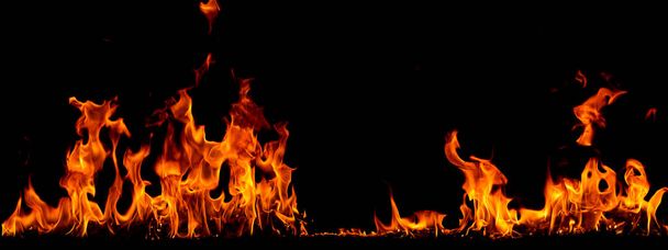 Στις φλόγες της φωτιάς στο μαύρο φόντο, καίγοντας κόκκινες σπίθες ξεσηκώνονται, φλεγόμενα πορτοκαλί λαμπερά ιπτάμενα σωματίδια - Φωτογραφία, εικόνα