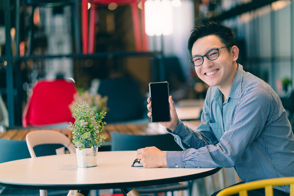 Asyalı iş adamı girişimci yeni mağaza ofis arka plan fikirlerinde el ile gülümseyerek akıllı telefon mutluluğunu gösterir - Fotoğraf, Görsel