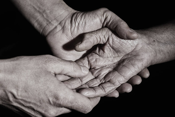 closeup of a young caucasian man holding the hand of an old caucasian woman with affection, in sepia tone - Photo, Image
