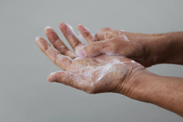 lähikuva valkoihoinen mies pesee kätensä saippualla vaalean harmaa tausta
 - Valokuva, kuva