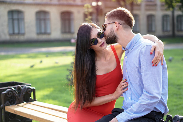 Beautiful couple of man and woman sitting on a bench in a park. Romantic theme with a girl and a guy. Spring Summer theme - Фото, зображення