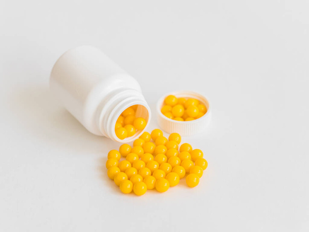Vitamins. Antiviral drug tablets. Round yellow healthy pills and pill bottle on white background. Minimalistic concept - Photo, image