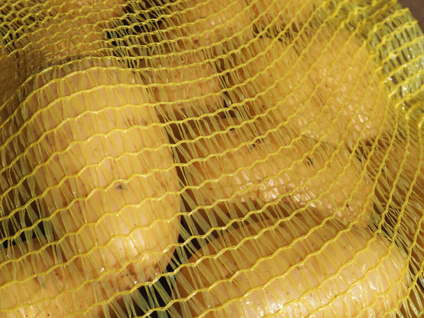 黄色いメッシュの袋の中のジャガイモ - 写真・画像