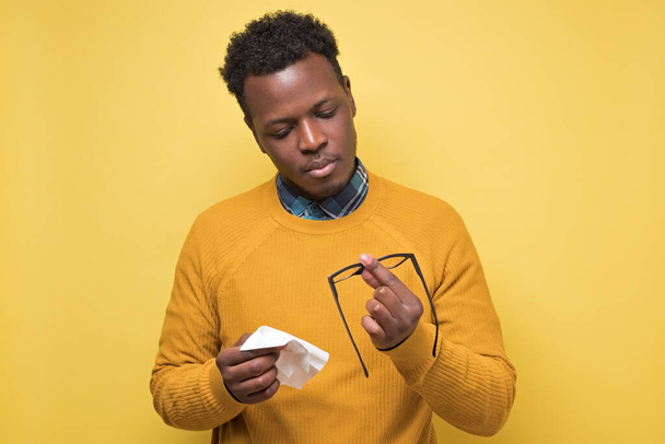 Young african american man in yellow clothes wiping his glasses isolated on colored background - Foto, Bild