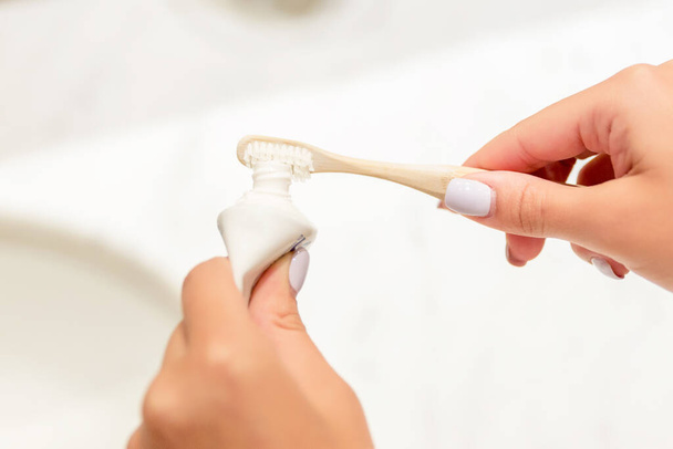 Kadın elinin banyodaki diş fırçasına diş macunu sürerken çekilmiş görüntüsü. Diş bakımı konsepti. Diş temizliği için hazırlık. - Fotoğraf, Görsel