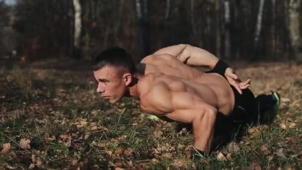 Mladý svalnatý sportovec cvičí kliky na jedné paži v lese. Silný běloch s nahým trupem - Záběry, video