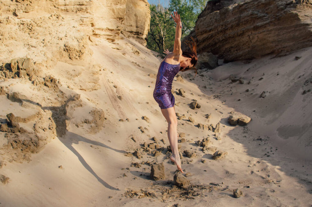 Ruskeahiuksinen nainen violetti kimalteleva mekko tanssia ja hyppäämällä hiekka rinteessä
 - Valokuva, kuva