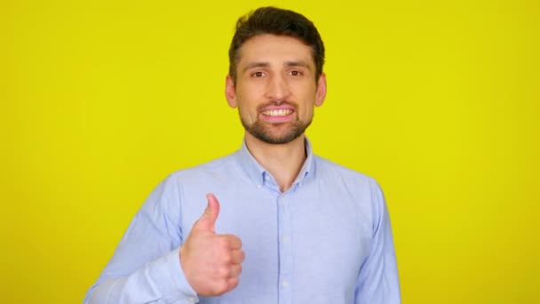 Young man in light blue shirt is smiling and shows thumb up, like. - Materiał filmowy, wideo