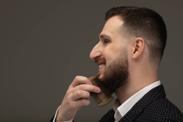 Young man comb his beard and moustache on gray background - Fotografie, Obrázek