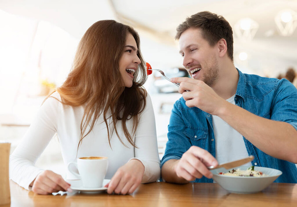 young couple handsome man feeds his beautiful woman with salad drinking coffee in cafe looking happy, relationship concept. - Foto, Bild