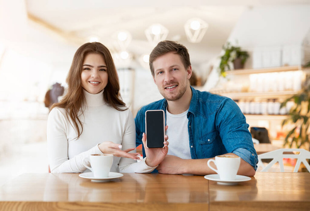 young couple beautiful woman and handsome man sitting at cafe during coffee break, she demonstrates new phone device, technology development concept. - Foto, Bild