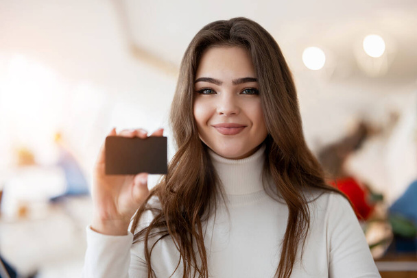 young brunette woman holding bank card looking satisfied, banking concept. - Foto, imagen