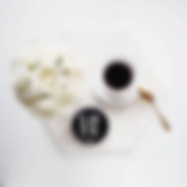 Blurry view of Flat lay Cup of coffee on wooden serving tray and flowers branch with macrame decoration. Minimal bohemian lifestyle concept for blog and social media - Foto, Bild