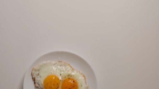 Two fried eggs on plate. Putting plate with fried eggs on wooden table. Close up white porcelain plate with fried egg. Traditional breakfast meal - Záběry, video