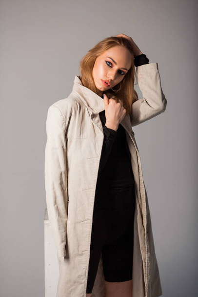 beautiful young woman with make-up in a light coat on a gray background - Fotoğraf, Görsel